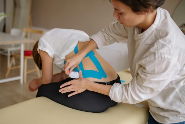 A physical therapist putting some kinetic tape on a patients back.