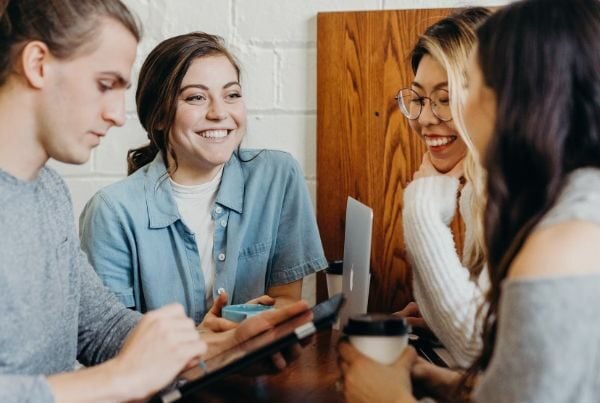 four young people talking and smiling while working together at a table