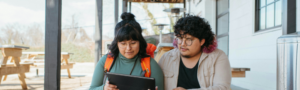 Two people siting on steps outside looking at a tablet.