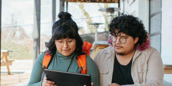 Two people siting on steps outside looking at a tablet.