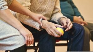 Caregiver supports a senior holding a therapy ball during rehabilitation